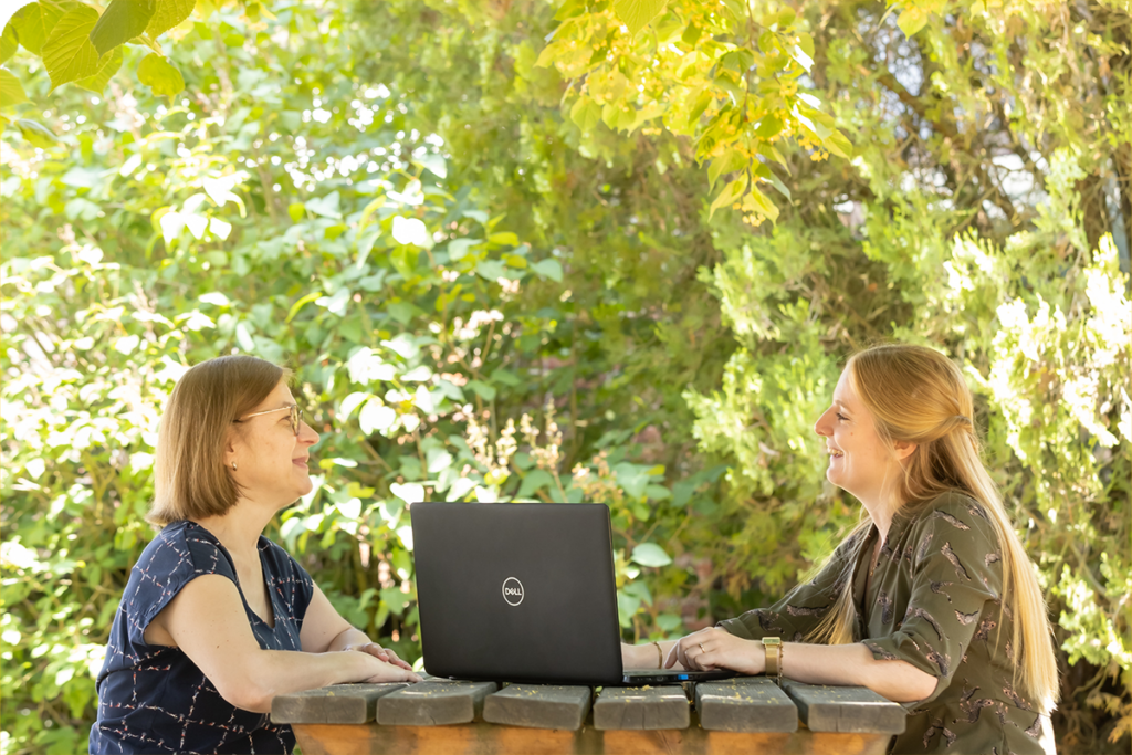 Twee personen zijn in gesprek aan een picknicktafel met een laptop tussen hen in